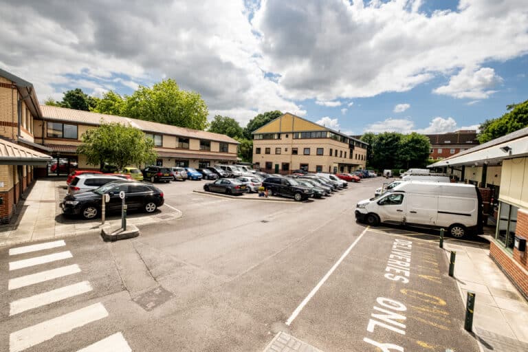 Car park with vehicles in parking spaces and office buildings in the background